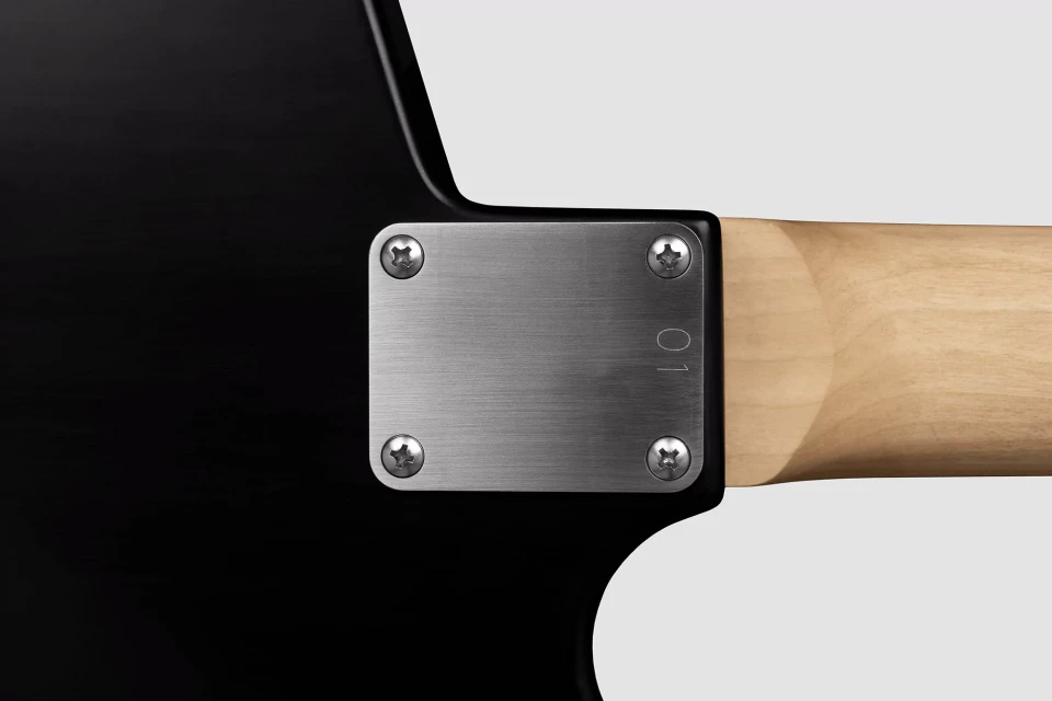 Close-up of the neck joint of a black electric guitar with a light-colored wooden neck, secured by a metal plate and four screws.