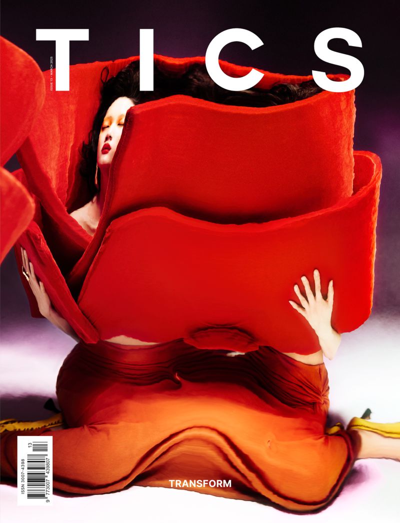 Fashion magazine cover featuring a woman with dark hair and red lips, partially enveloped in a large red rose-like sculptural garment.