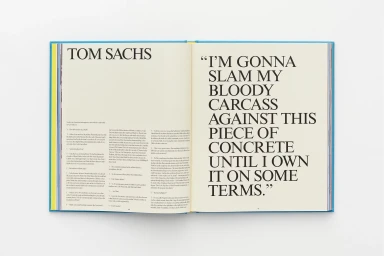 Open hardcover book titled Tom Sachs showing bold typography on off-white paper against a clean white surface
