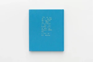 A blue fabric hardcover book with embroidered white text on the front cover, resting against a plain white background.