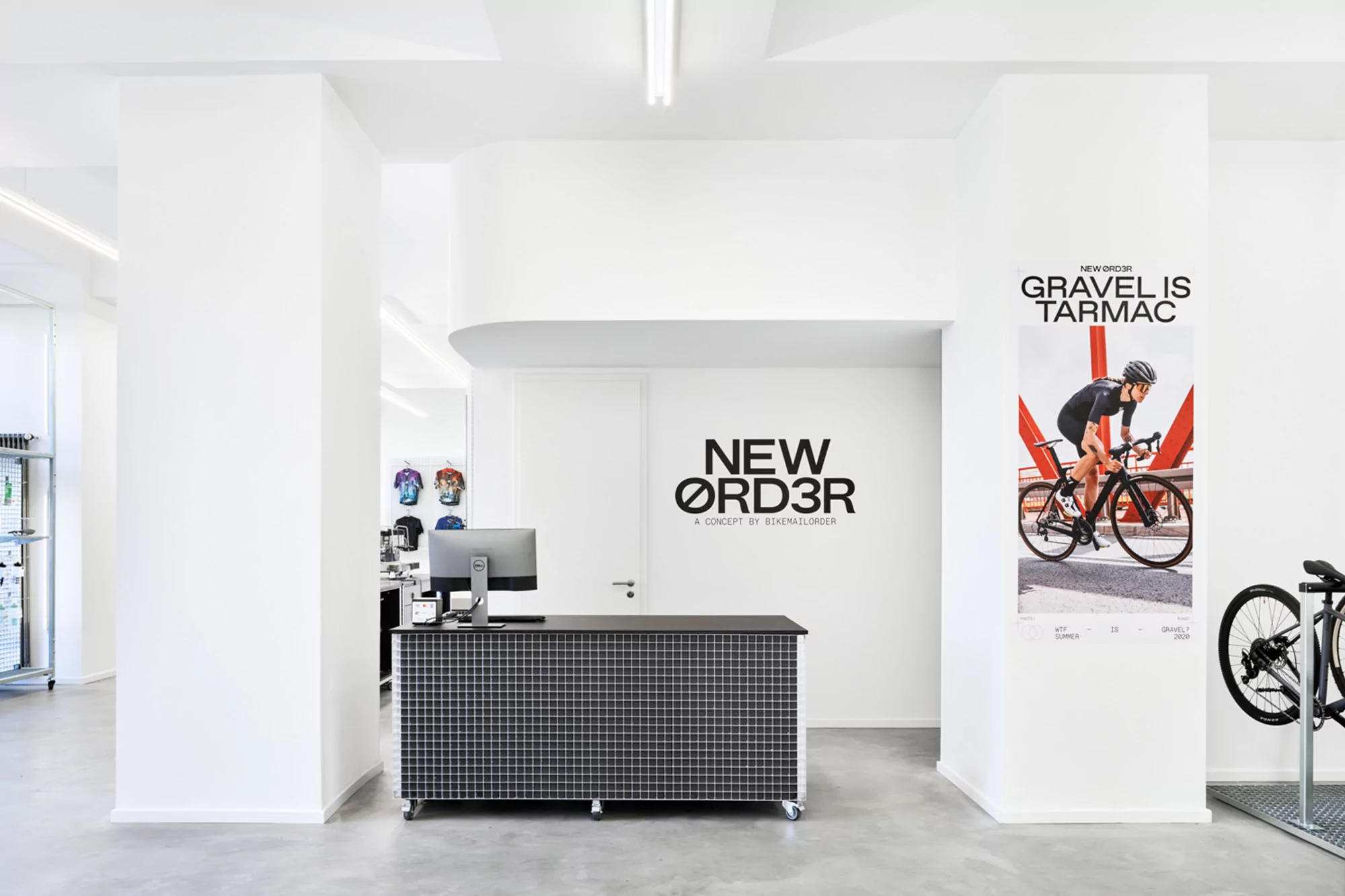 Bright, modern bike shop interior with a black reception desk, computer, bike poster, and partial bicycle in a clean, minimalist space.