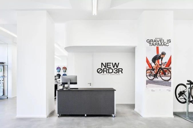 Bright, modern bike shop interior with a black reception desk, computer, bike poster, and partial bicycle in a clean, minimalist space.