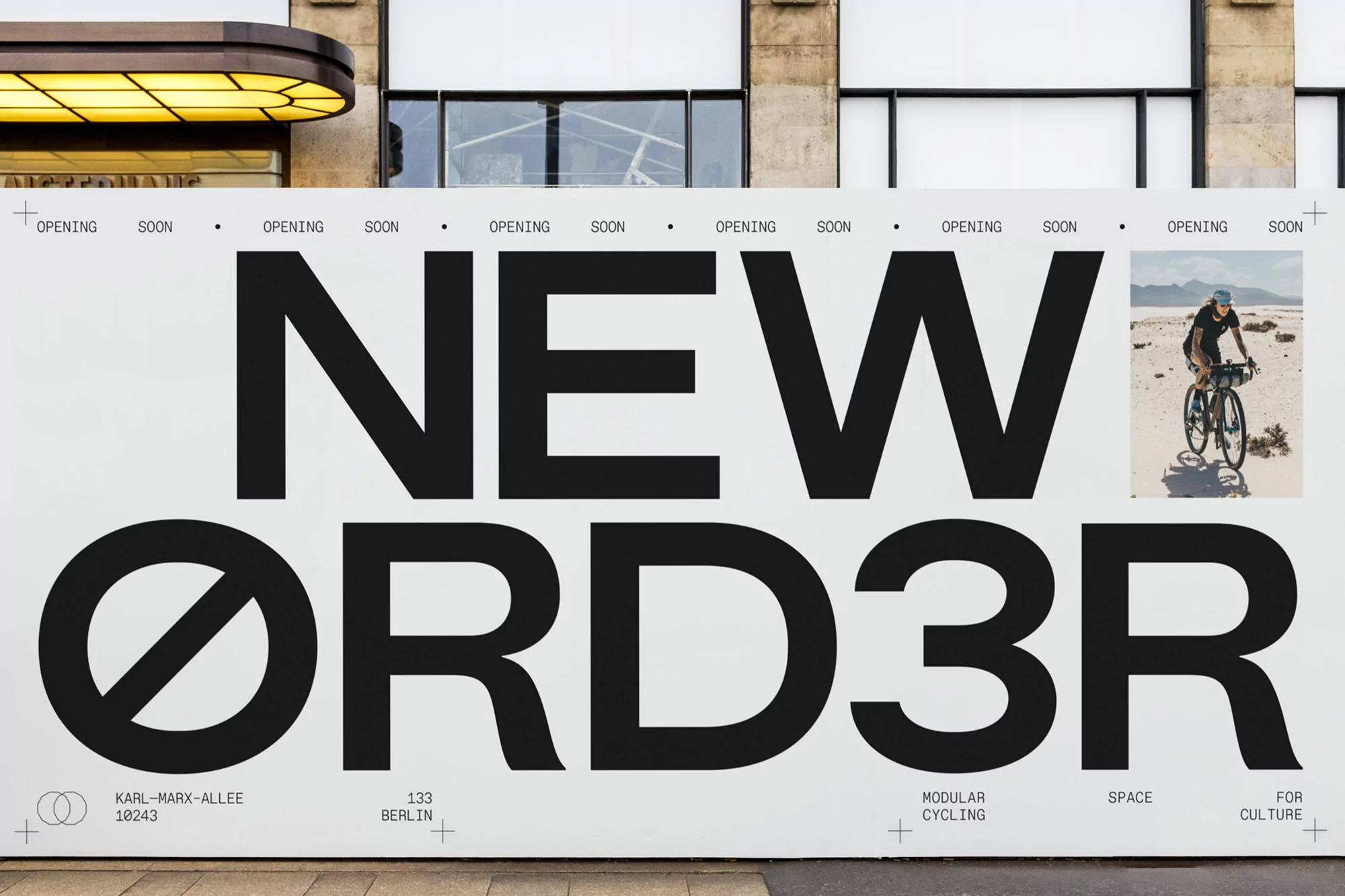 Advertising for New Order modular cycling space in Berlin with cycling image. Bold text on a white wall; street-level view.