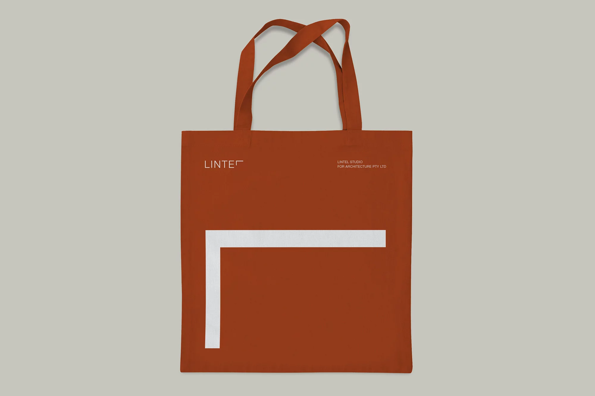 Studio shot of a tote bag in a neutral setting, featuring an earth-tone color, white text, and a simple line design element.