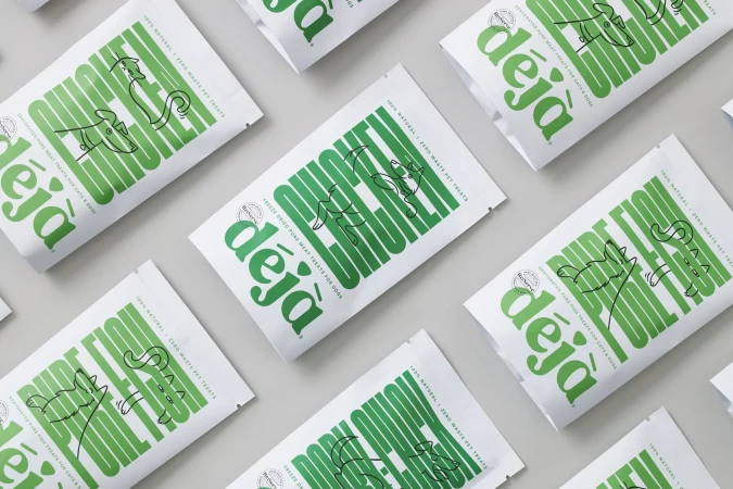 Overhead shot of multiple white bags of Déjà pet treats, featuring illustrated animals and green typography, arranged on a light gray surface.