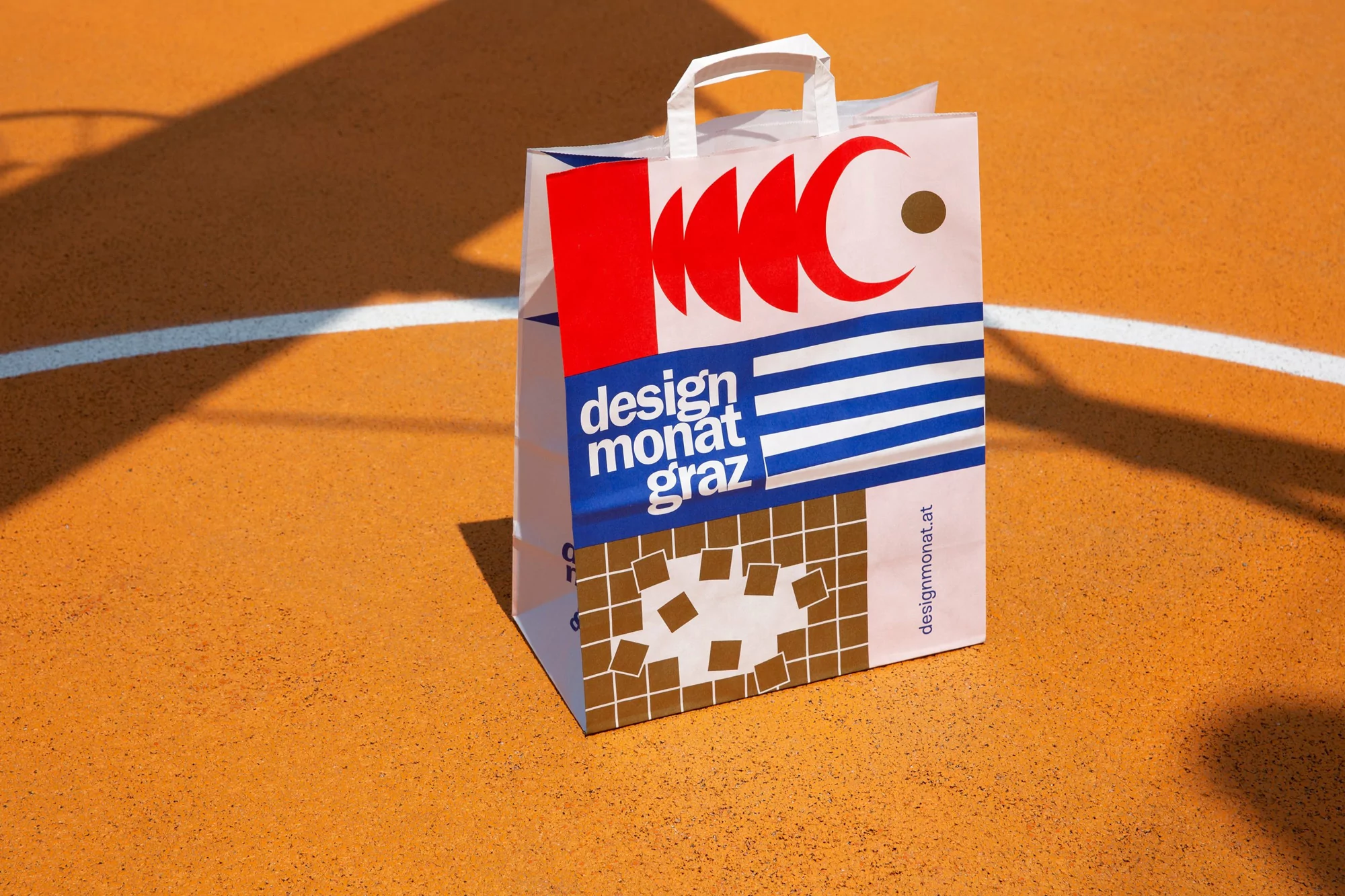 Shopping bag on an orange surface with graphic designs in red, white, blue, and brown, casting a shadow from the side.