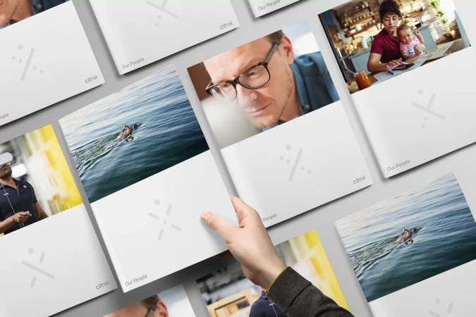 Hand holding a selection of corporate brochures featuring people, water, and tech-themed images. The brochures are angled on a plain surface.