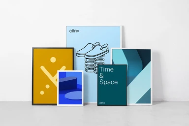 Collection of framed posters and graphic art prints leaning against a plain white wall on a concrete floor