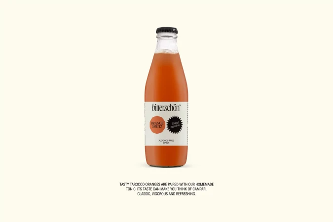 A bottle of orange spritz drink with a black cap and clear label on a light beige background. Refreshing non-alcoholic drink.