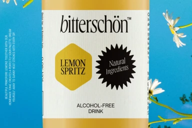 Product label for Bitterschön lemon spritz alcohol-free drink set against a bright blue background with daisy flowers.