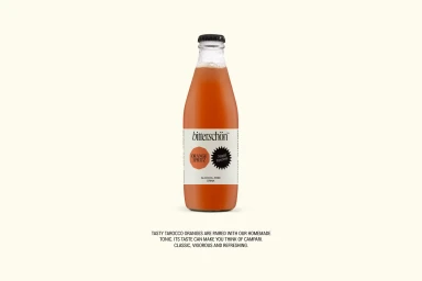 Glass bottle of orange spritz beverage with a black cap and cream label against a plain light background