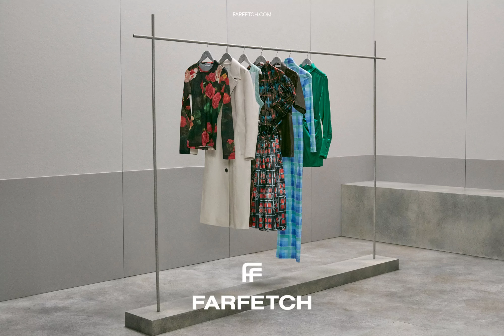Fashion apparel on a metal clothing rack includes dresses, tops, and a cream-colored coat in a minimalist studio setting.