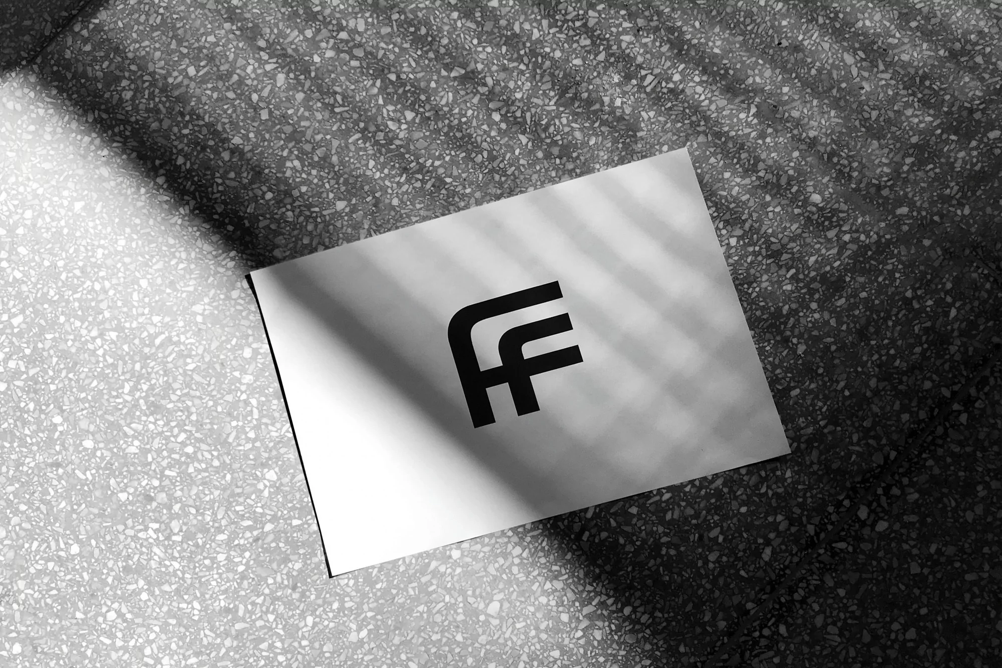 A white card with a black 'FF' logo rests on a textured gray surface, illuminated by a beam of window light and shadows.