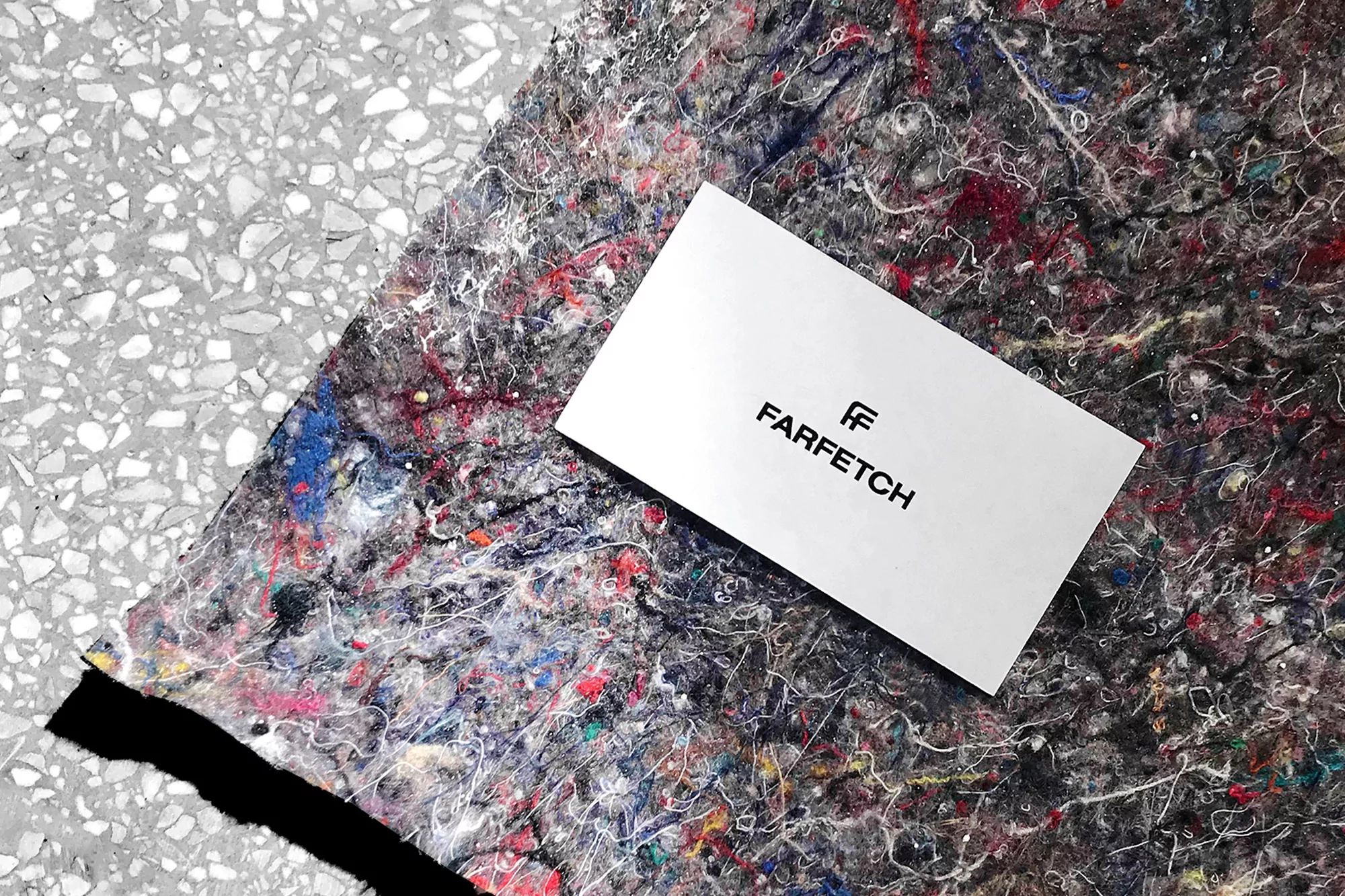 Farfetch logo on a white card resting on a textured surface with splatters of color and a gray stone-like background.