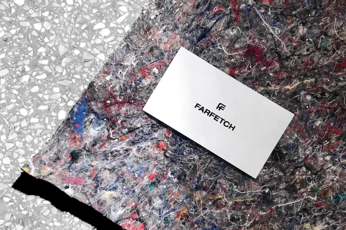 Farfetch logo on a white card resting on a textured surface with splatters of color and a gray stone-like background.