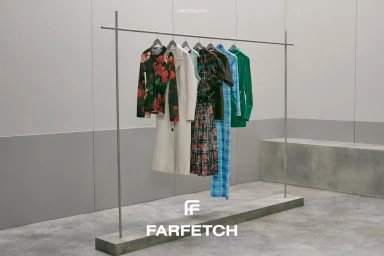 Minimalist clothing rack holding several colorful garments against a concrete showroom background for Farfetch