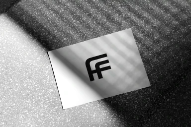 White card featuring the Farfetch FF logo resting on a textured grey speckled terrazzo surface with striped shadows