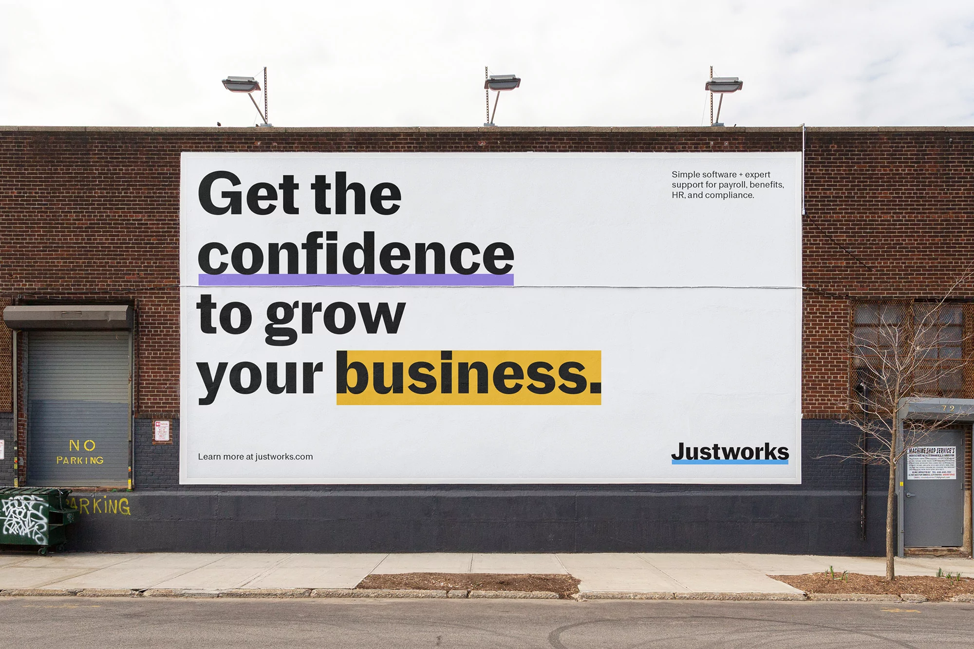 Billboard on a brick building promotes business growth with the Justworks logo; urban setting with a sidewalk and street.