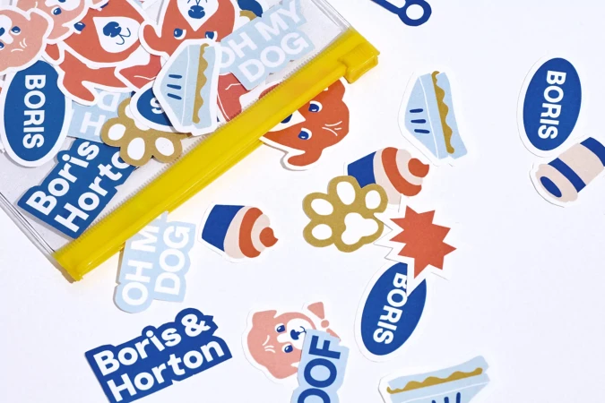 Flat lay of die-cut dog-themed stickers including cartoon dogs, dog food, and Boris & Horton logo stickers on a white backdrop.