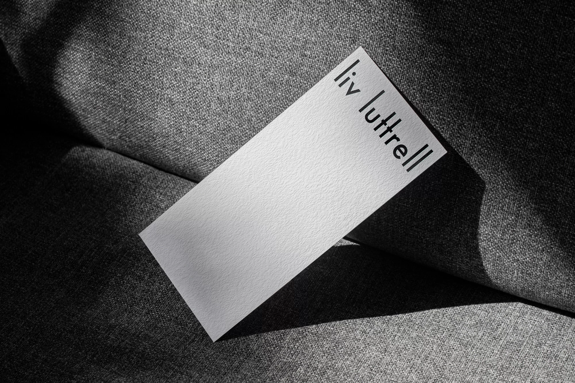 Close-up of a white business card with black sans-serif text on a gray textured surface, lit with dark shadows, portrait orientation.