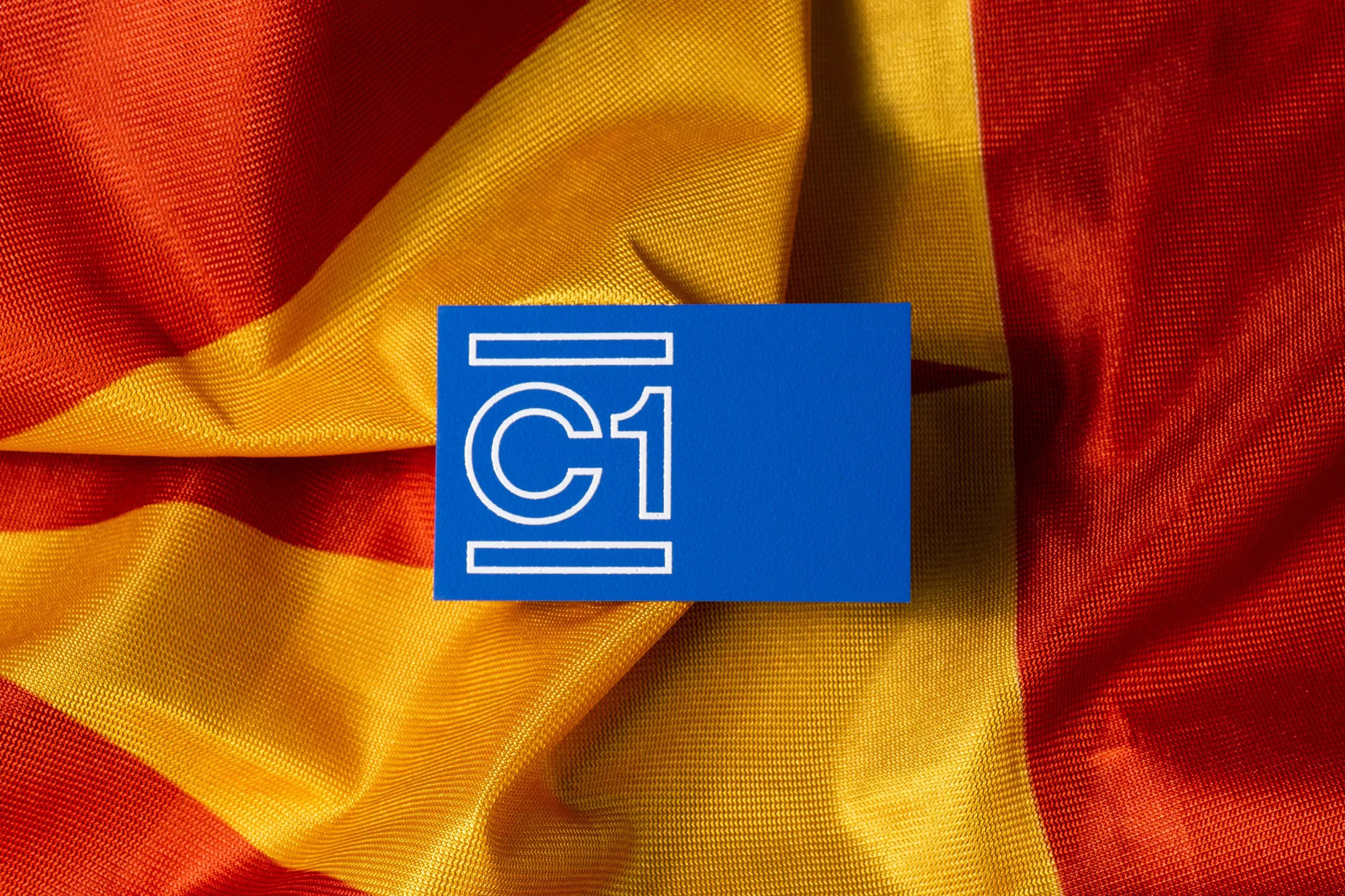 Close-up of a blue card with a white C1 logo on a textured fabric background in red and yellow hues, creating a vibrant backdrop.