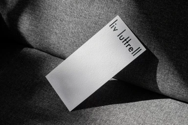 White textured business card with black text reading liv luttrell resting diagonally on a dark grey fabric surface