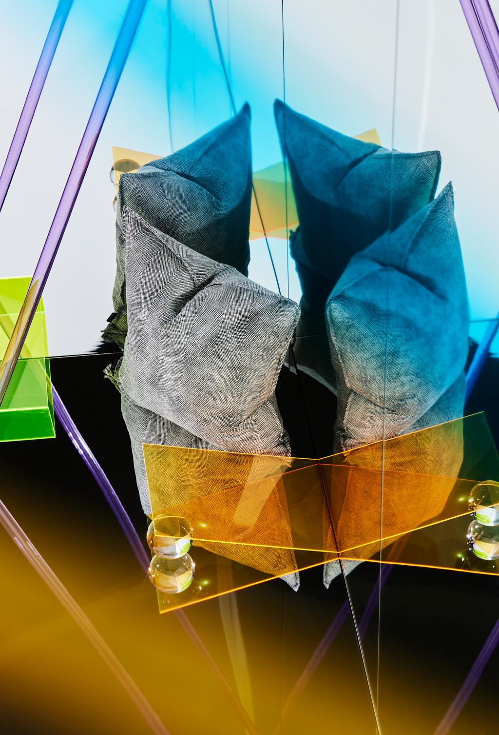 Abstract sculpture features two folded gray textile forms above transparent amber glass on a black surface with vibrant neon highlights.