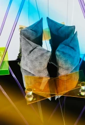 Grey textured cushions reflected in geometric mirrors with transparent amber, blue, and green acrylic panels
