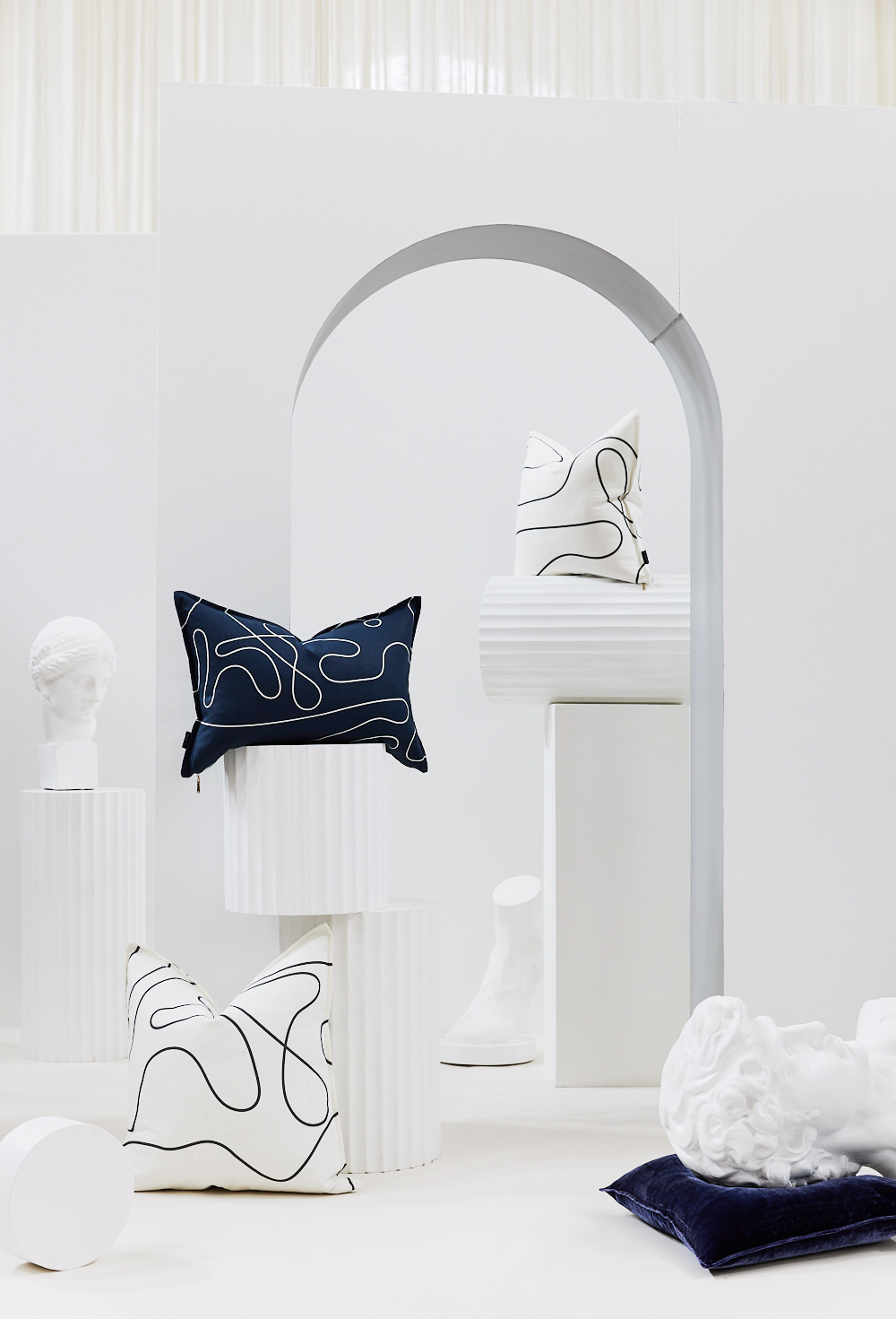 Stylish interior studio shot featuring a collection of graphic pattern throw pillows displayed alongside classic white busts on columns.