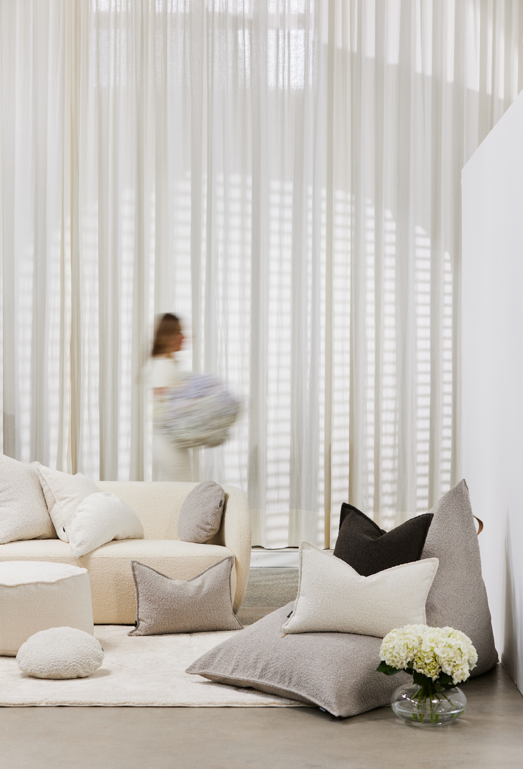 Neutral-toned interior with a cream couch, decorative pillows, white shag rug, and vase of white hydrangeas, bathed in natural light.