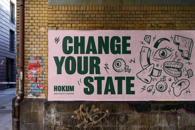 Street art poster on a brick wall features an illustrated face and text, 'Change Your State' advertising Hokum Speciality Coffee.