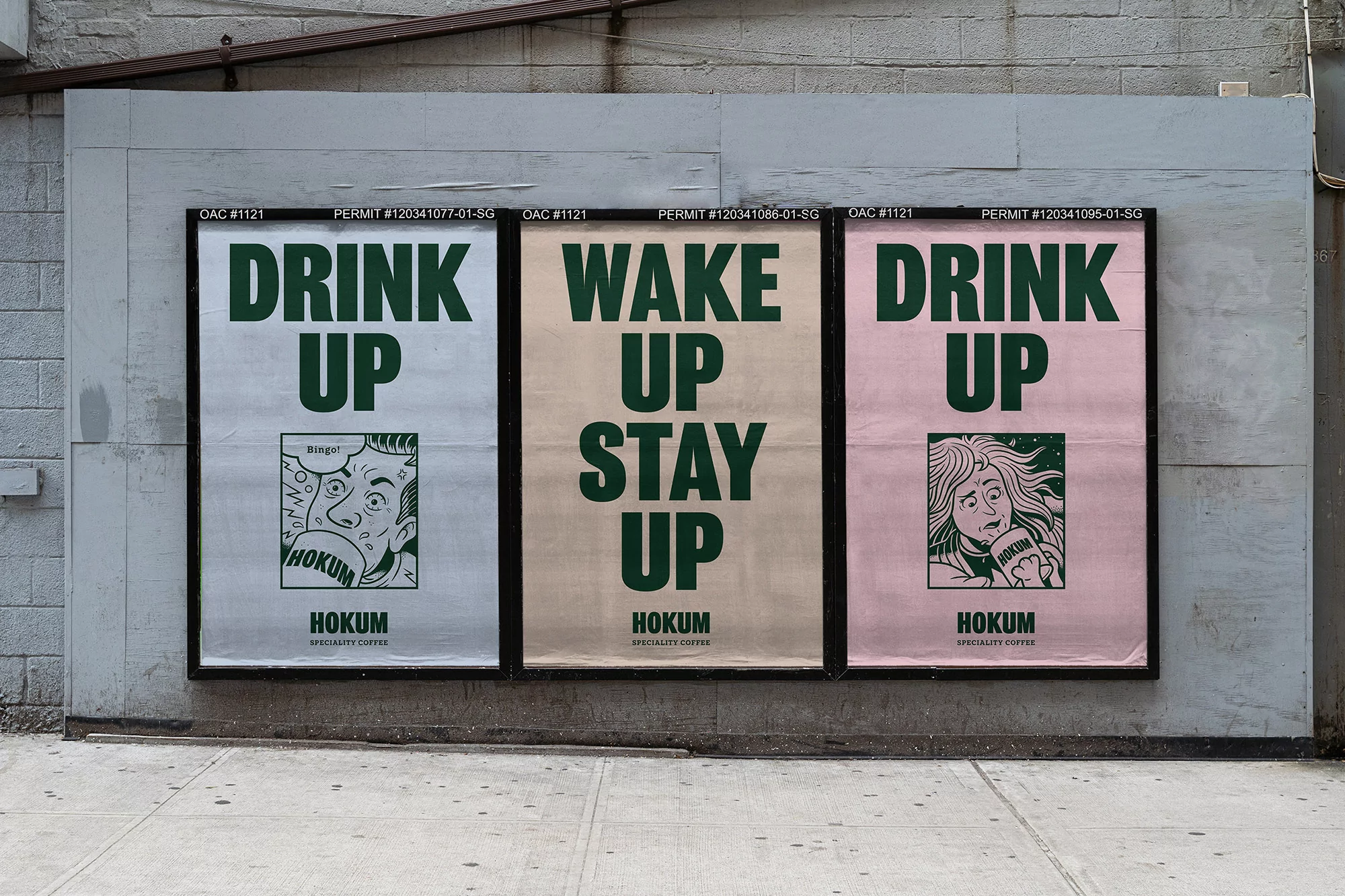Eye-level shot of three HOKUM specialty coffee advertisements on a gray exterior wall, promoting 'Drink Up' and 'Wake Up Stay Up'.