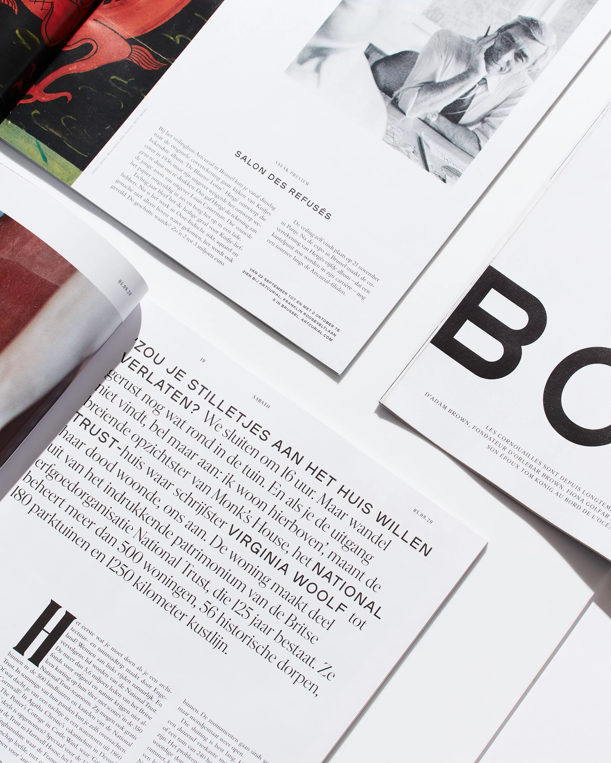 Various open magazines on a white surface display articles, text, and an illustration. The lighting is bright and even, creating a clean, minimalist aesthetic.