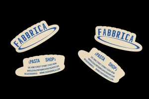 Fabbrica brand identity stickers with blue typography on cream backgrounds set against a solid black background.