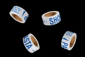 Four rolls of branded adhesive tape with blue typography floating against a solid black background.