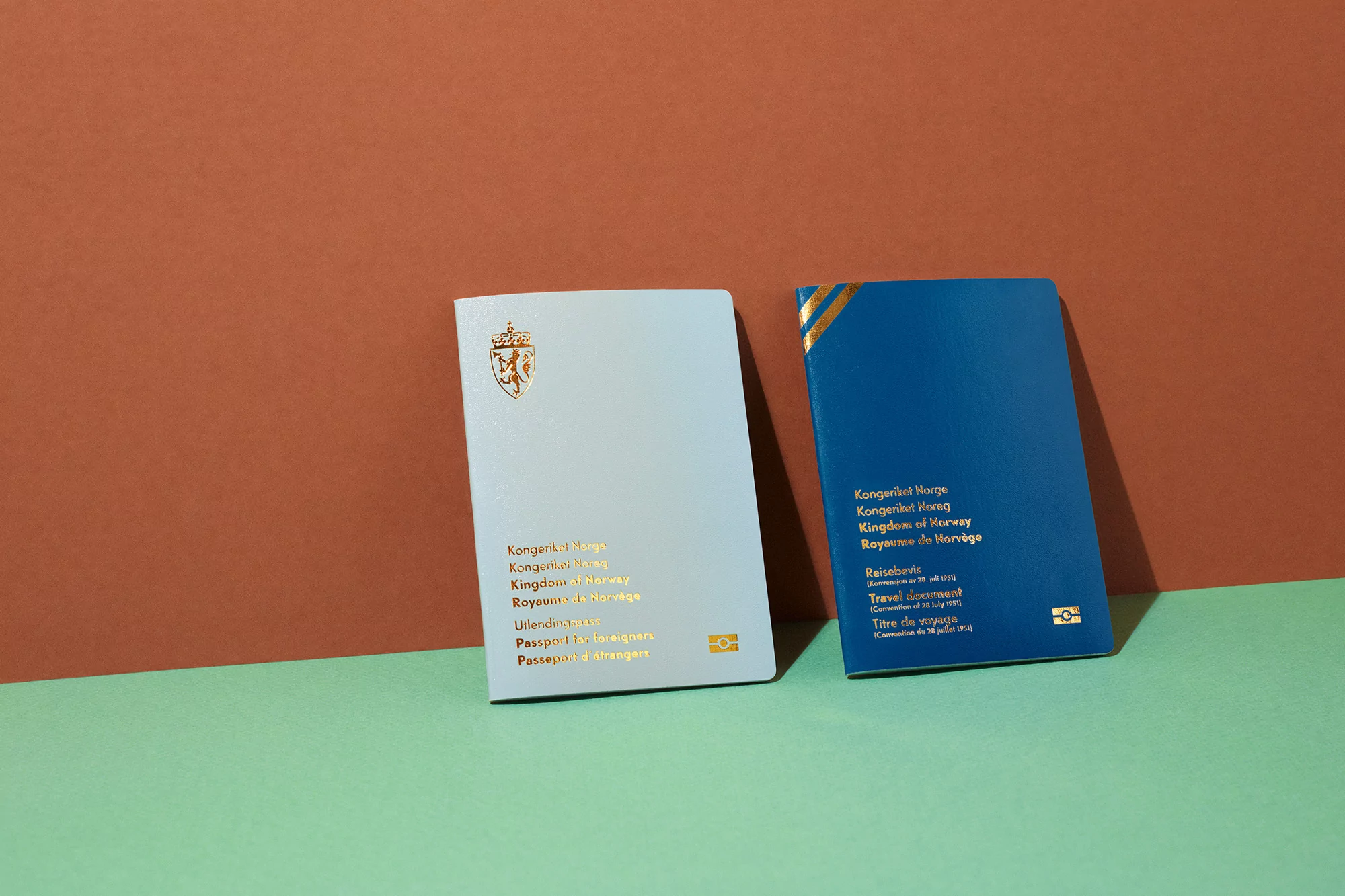 Two passports of Norway, one light blue and one dark blue, sit against a background of red-brown and light green. Travel document.