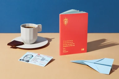 Red Norwegian passport, national ID card, coffee cup, chocolate, and paper airplane on a tan and blue surface.