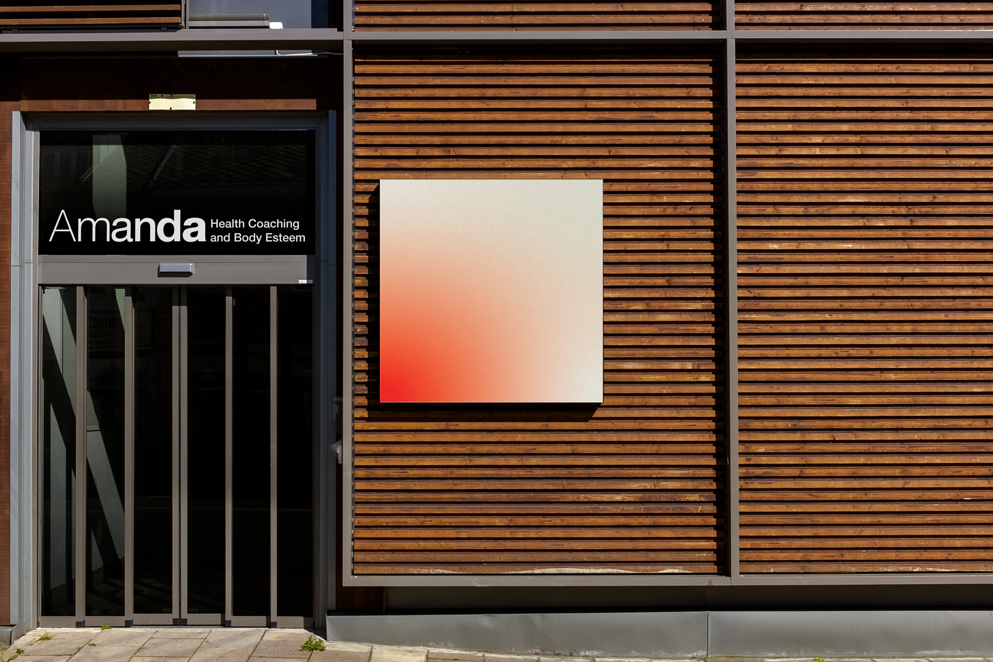 Exterior view of modern building with wooden facade, gray door, and a sign that reads Amanda Health Coaching and Body Esteem.