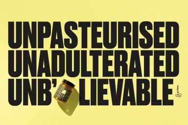 A small jar of honey resting on a pale yellow background beneath bold black uppercase typography reading unpasteurised unadulterated unbelievable