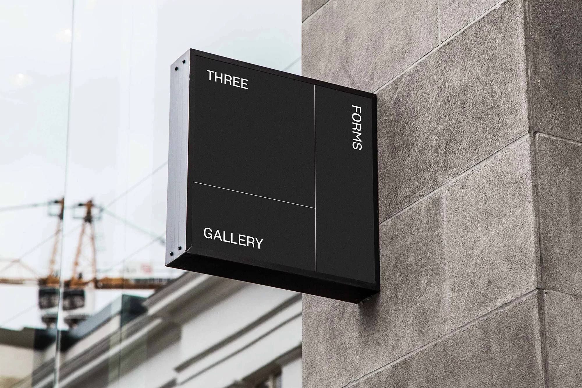 Exterior of Three Forms Gallery, featuring a modern black sign with white text on a grey stone wall, architectural backdrop with crane.