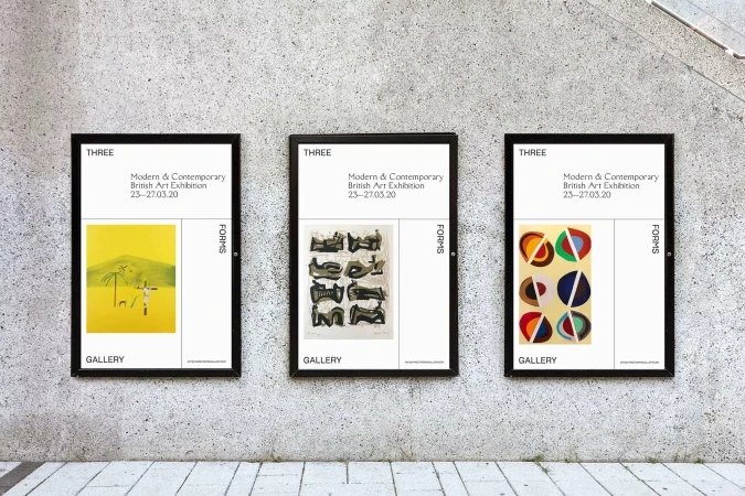 Three framed art posters displaying a modern British art exhibition hang in a row on a grey concrete wall inside an art gallery.