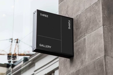 Black rectangular sign with Three Forms Gallery branding mounted on a textured stone wall exterior.