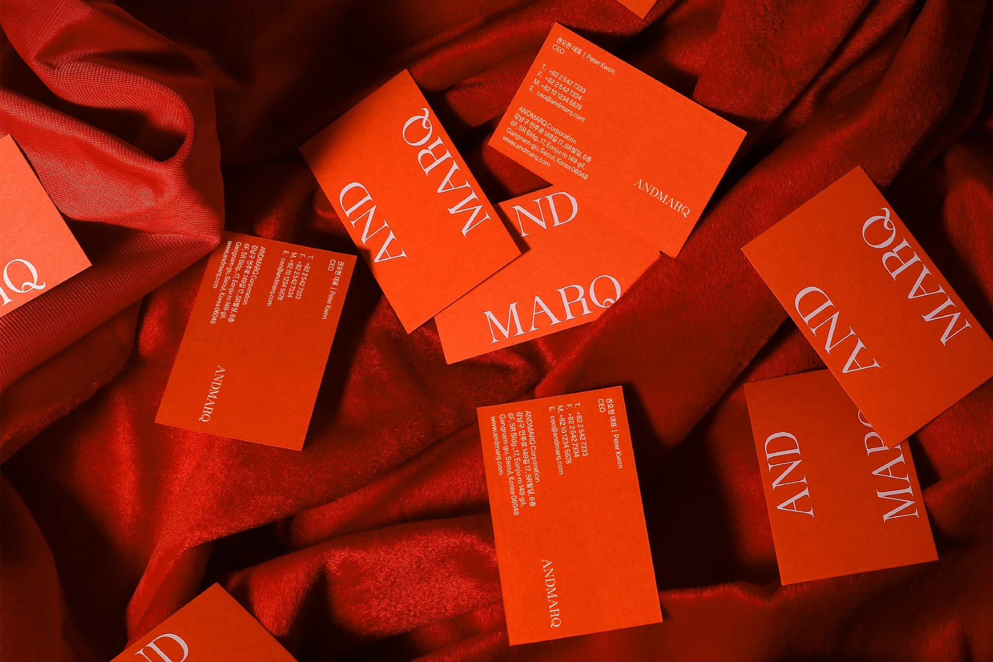 Stack of coral ANDMARQ business cards with white sans-serif typeface branding set against a rumpled, shiny dark coral fabric.