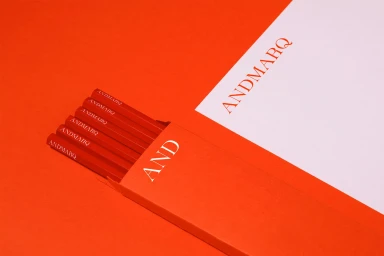 Red branded stationery set featuring pencils and paper with the ANDMARQ logo against an orange background