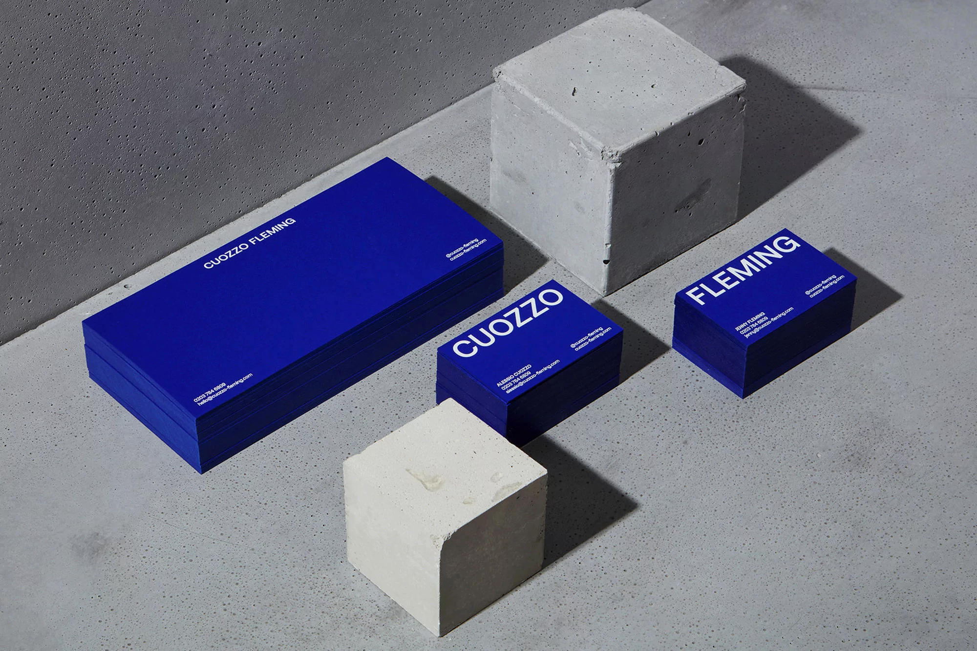 Stacks of Cuozzo Fleming business cards in blue and concrete cubes on a gray surface, professional branding and design concept.