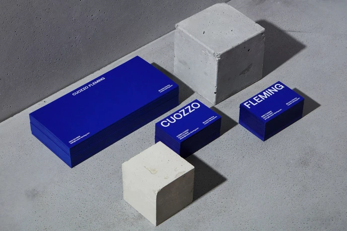 Blue business cards and stationery pieces arranged with concrete blocks on a grey textured surface.
