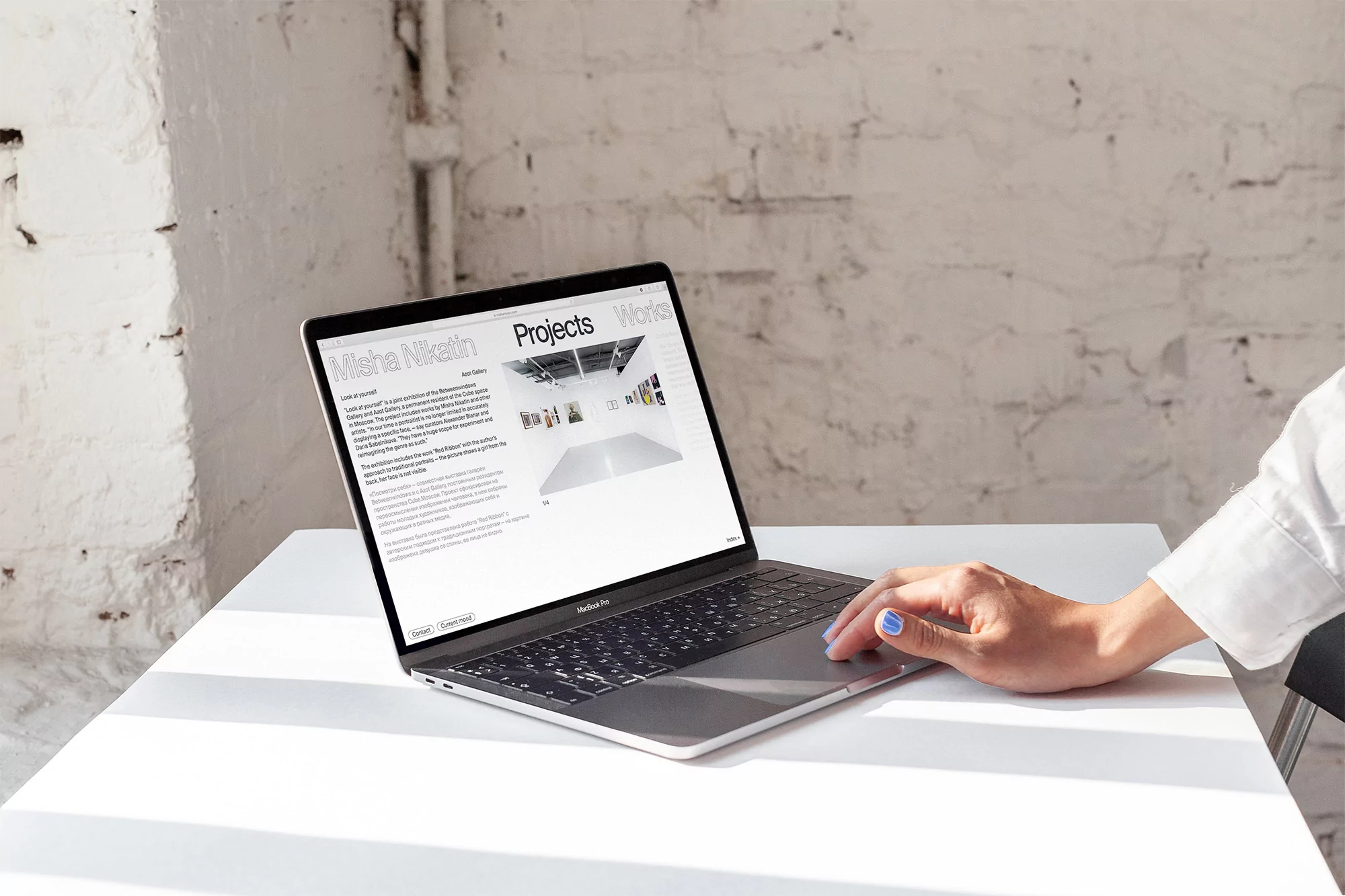 Laptop on white table with a person's hand using the trackpad, displaying a website with an interior design project showcase.