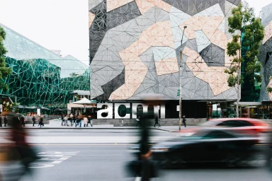 ACMIs geometric patterned building exterior with blurred cars and pedestrians on a street