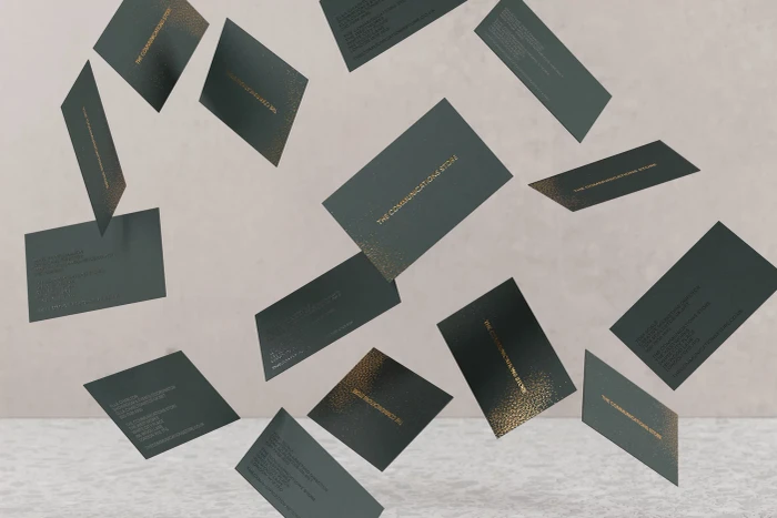 Dark green business cards with gold foil typography floating against a light textured background