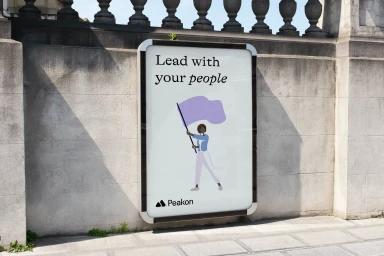 An outdoor billboard poster mounted on a stone wall, featuring typographic design and an illustrated figure holding a flag for Peakon.